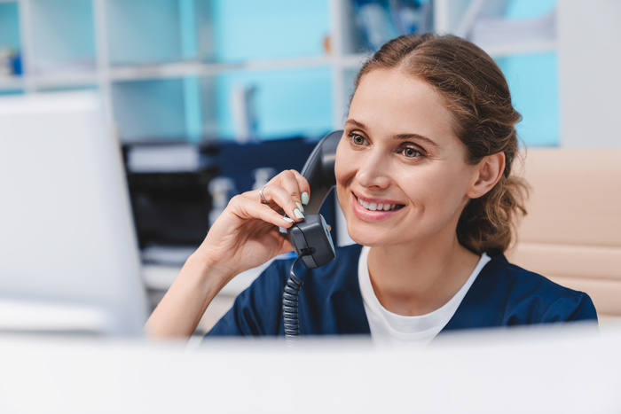 Young female nurse working at reception desk while answering phone calls and scheduling appointments