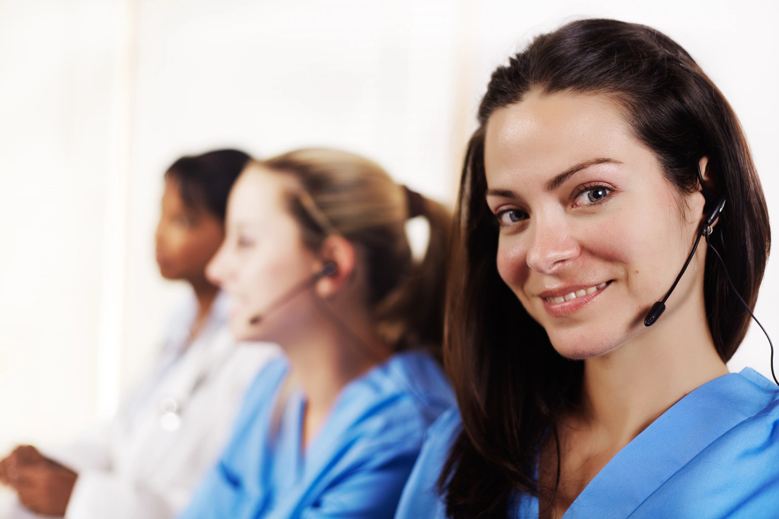 Woman in medical attire smiling, wearing a headset.