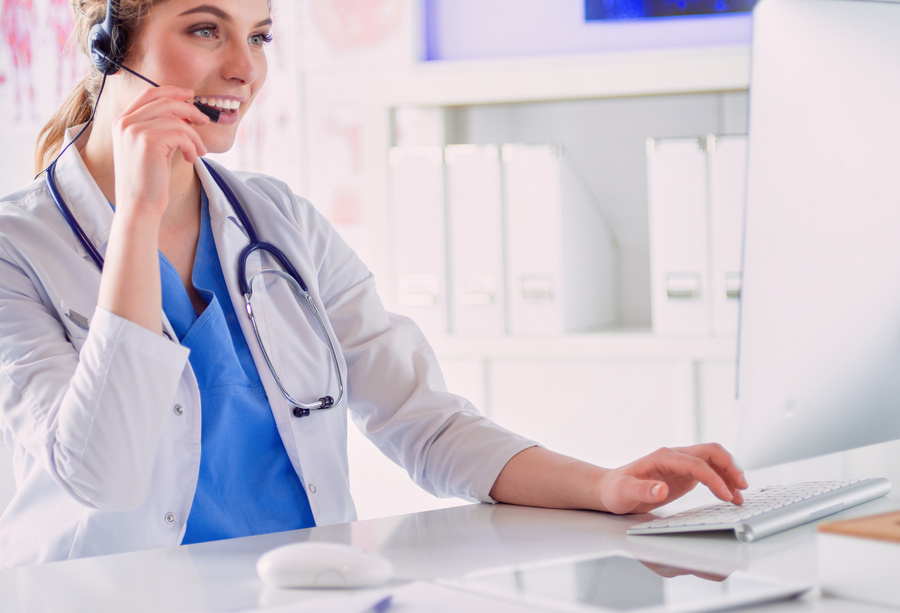 Young practitioner doctor working at the clinic reception desk, she is answering phone calls and scheduling appointments